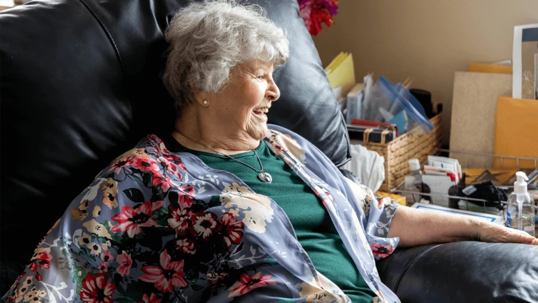 An elderly lady smiling and watching outside the window while sitting on sofa