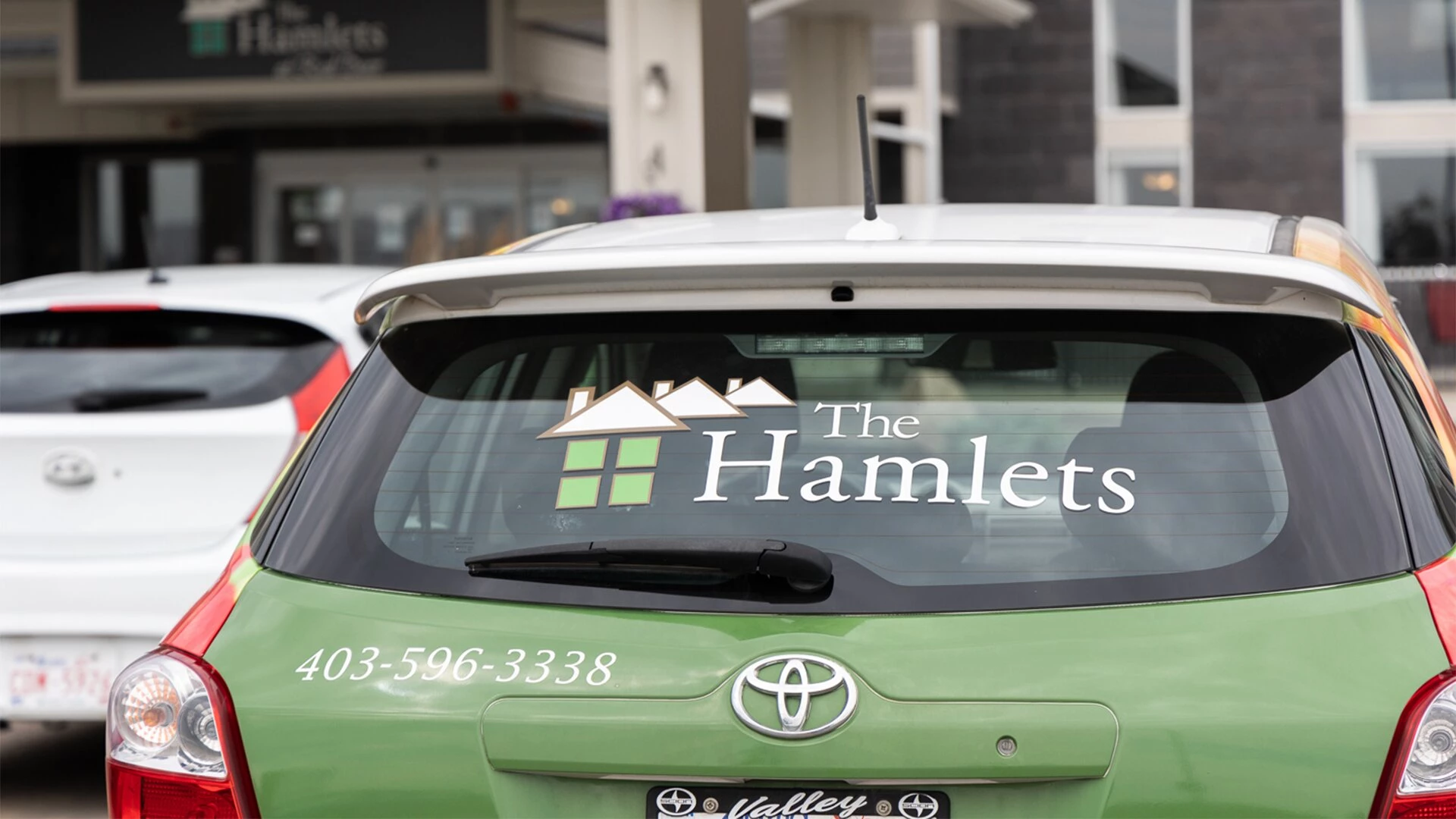 A green hatchback car with The Hamlets of Red Deer name and number